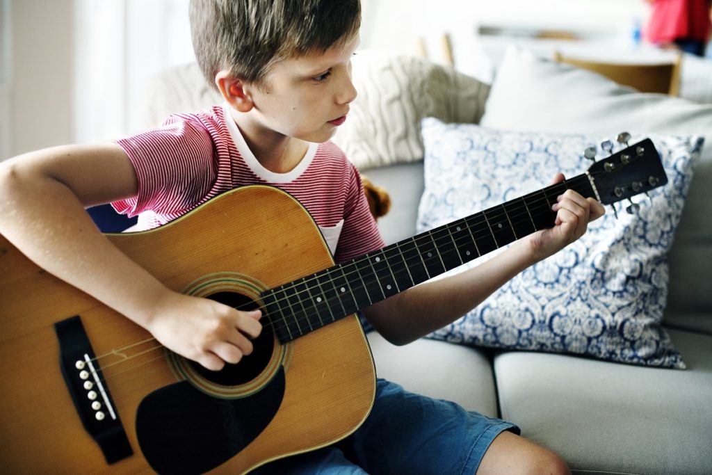 Junge sitzt auf einem Sofa und spielt Gitarre